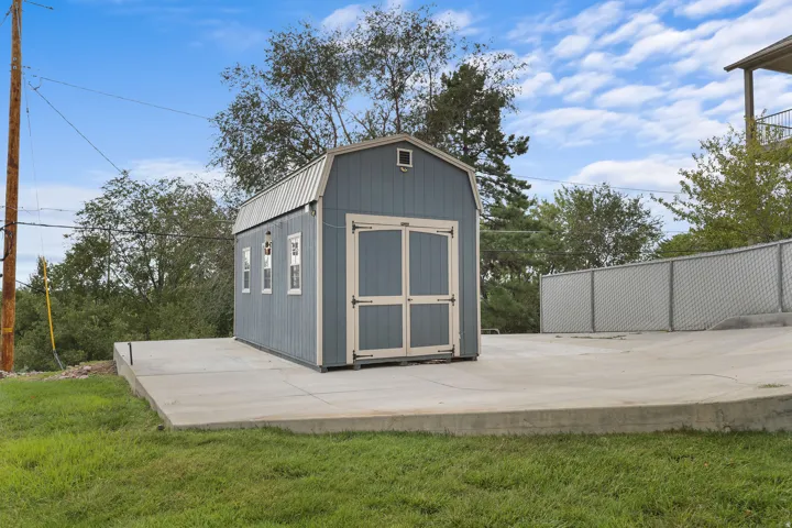 Detached utility shed with a gambrel roof and multiple windows, positioned on a concrete pad