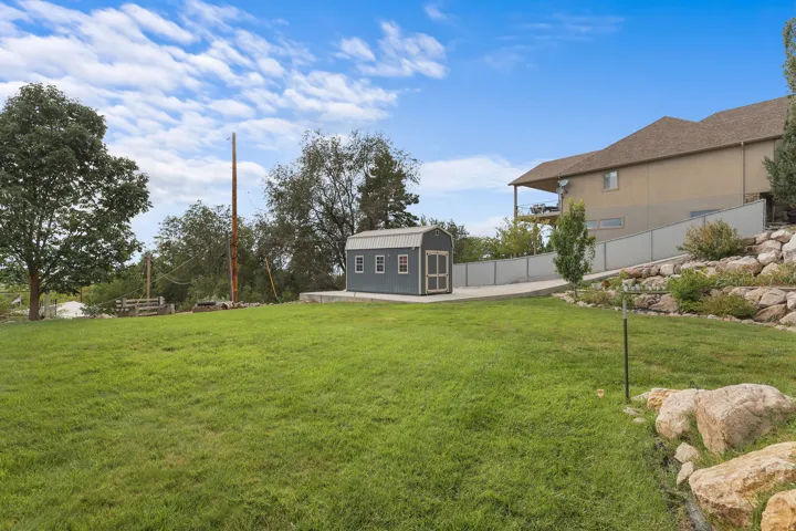 Expansive grassy yard with a built storage shed, concrete pathway, and tiered rock landscaping