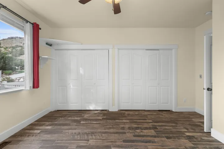 Wood-finish flooring, two sets of bi-fold closet doors, a ceiling fan, and a window with a mountain backdrop