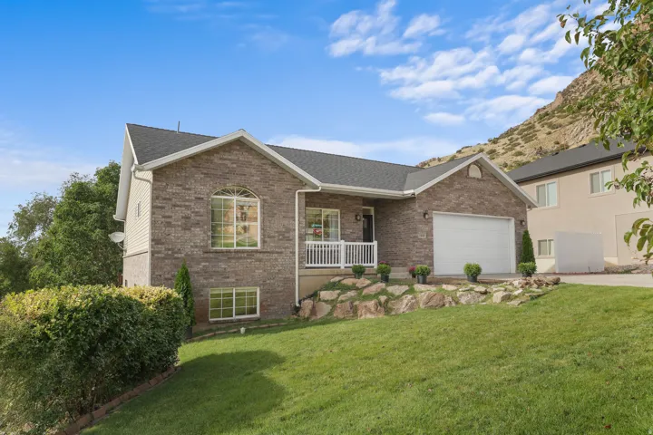 Brick exterior with white trim, arched window, white garage door, front porch with white railing, and sloped grassy lawn