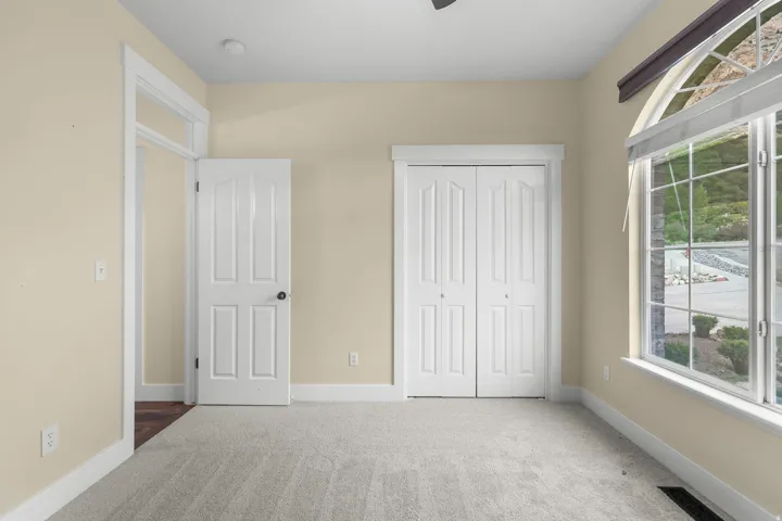 Arched window with gridded panes, light-colored carpeting, white paneled doors, and bi-fold closet doors