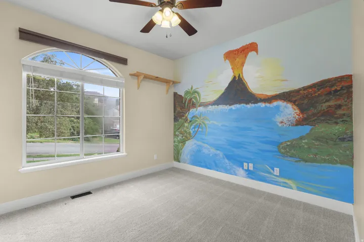Arched window with gridded panes, ceiling fan with integrated lighting, wall mural, and light-toned carpeting