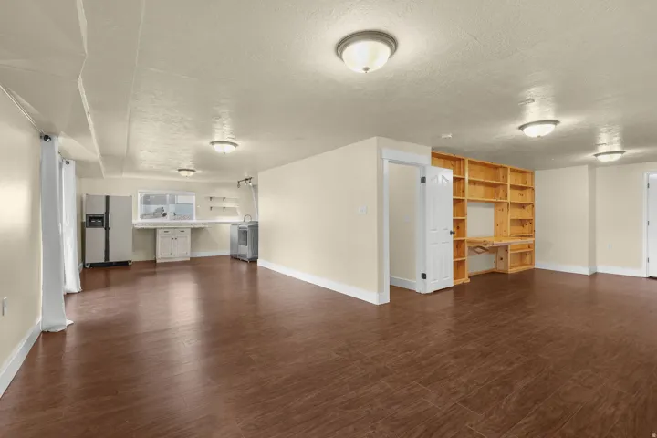 Spacious open-concept room featuring wood-finish flooring, recessed lighting, built-in shelving with integrated desk, and a utility area with a sink and cabinetry