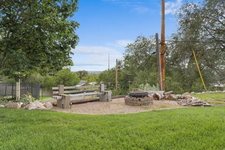 Expansive grass area, concrete bench seating, paver fire pit, mature trees, and a distant landscape