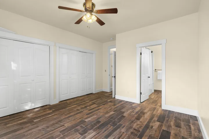 Wood-finish flooring, two sets of bi-fold closet doors, ceiling fan with integrated lighting, and a white paneled door