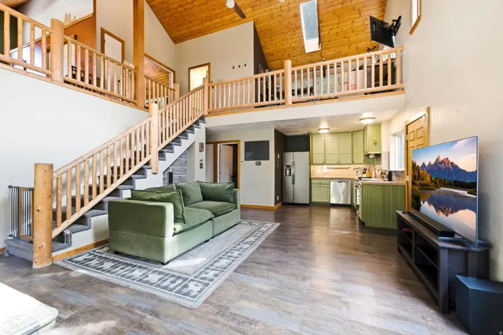 Vaulted wood-finish ceilings with skylights, wood-finish flooring, custom wood staircase and railings, green cabinetry, and stainless steel appliances