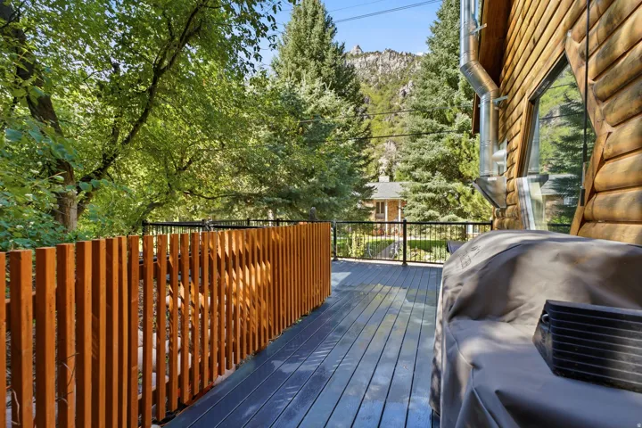 Expansive outdoor deck with dark composite decking, a wood-slat privacy screen, black metal railings, and a log-cabin exterior