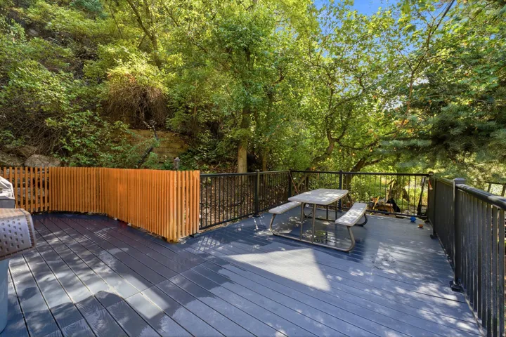 Spacious outdoor deck with dark wood-finish flooring, black metal railings, and a natural wood privacy screen, surrounded by mature trees