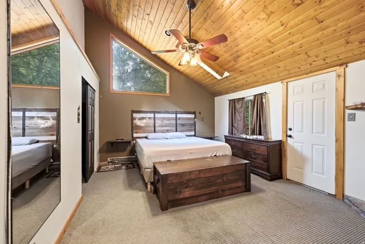 Vaulted wood-paneled ceiling, ceiling fan, carpeted flooring, triangular window, and a paneled door