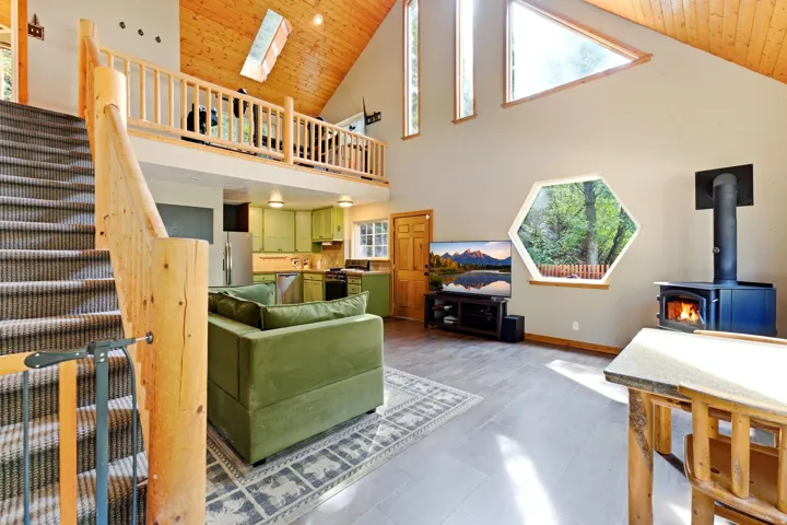 Vaulted wood-paneled ceiling with skylight, exposed wood beam staircase, hexagonal window, wood-burning stove, and upper-level loft
