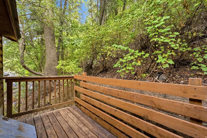 Private wood deck with wood slat railing, surrounded by mature trees and lush foliage