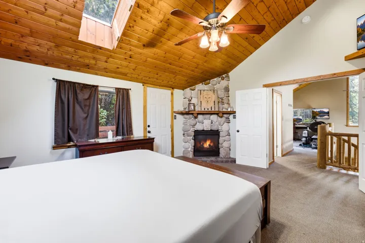 Vaulted wood-paneled ceiling with skylight, stone-clad fireplace, ceiling fan, and wood trim accents