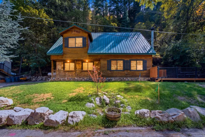 Log cabin exterior with a green metal roof, a covered front porch, and a side deck