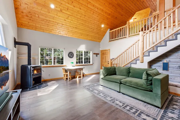 Vaulted wood-paneled ceiling, wood-finish flooring, wood-burning stove, natural wood staircase with log railings, and multiple windows