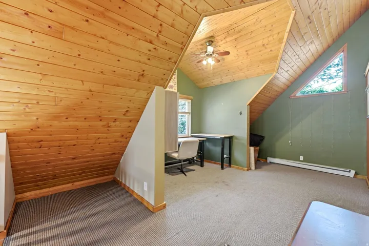 Wood-paneled vaulted ceilings, an angular window, ceiling fan, and carpeted flooring
