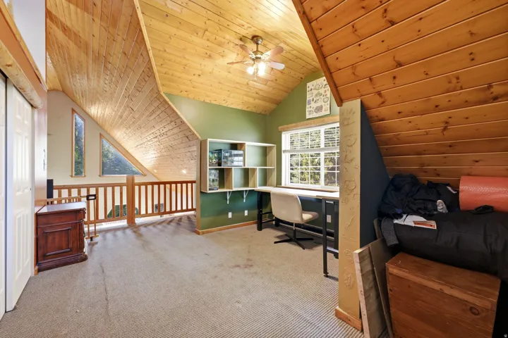 Vaulted wood-paneled ceilings with ceiling fan, built-in shelving, wood railing, and window with blinds