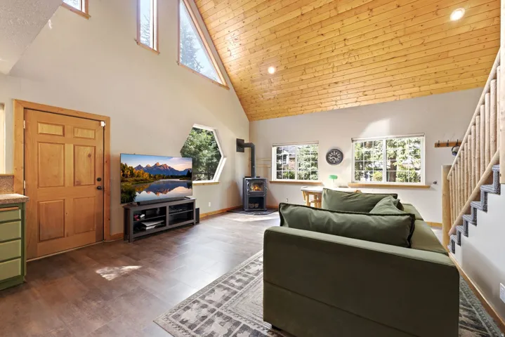 Vaulted wood-paneled ceiling, wood-finish flooring, multiple windows, wood-burning stove, and a wood staircase with railing