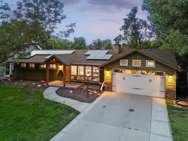Gable roofline with solar panels, covered front entry, attached garage with decorative hardware, stone accents on exterior walls, and a concrete driveway