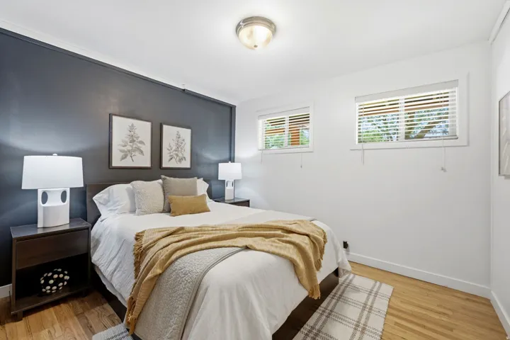 Hardwood flooring, two windows with blinds, flush mount ceiling light, and a dark accent wall