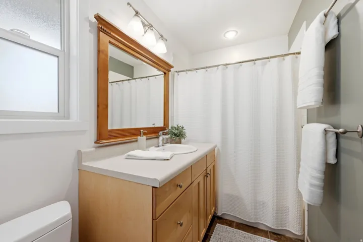 Wood-finish vanity with two inset sinks, stone-finish countertop, and a large wood-framed mirror