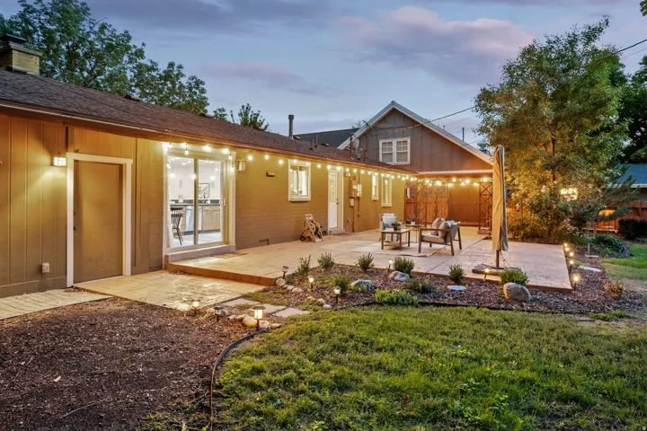 Expansive backyard concrete patio with integrated landscape lighting, mature trees, and a sliding glass door entry