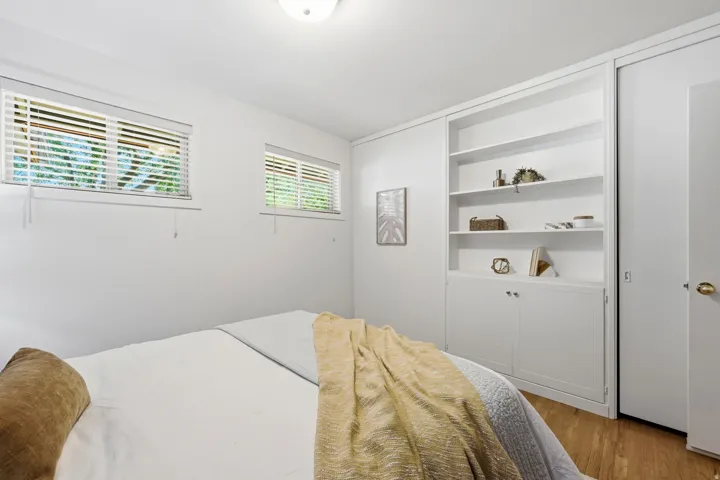 Recessed lighting illuminates the room, featuring two windows with horizontal blinds, built-in shelving, and wood-finish flooring