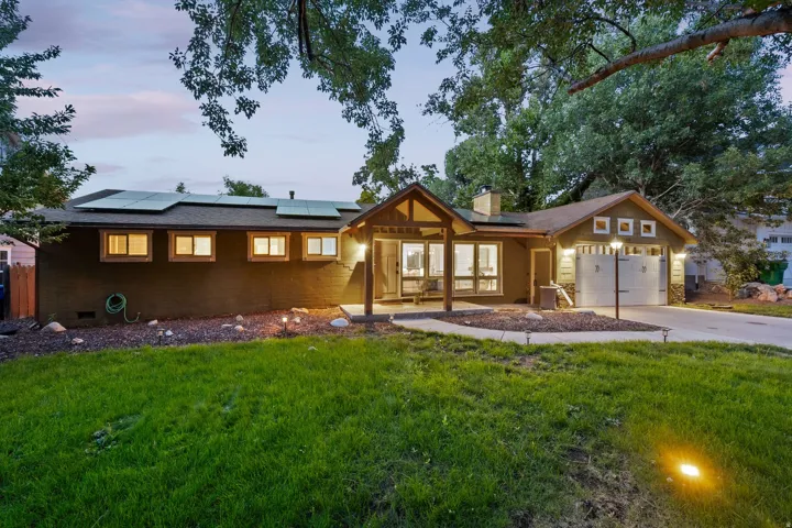 Expansive front lawn with walkway lighting, attached two-car garage, solar panels, covered entryway, and multiple large windows