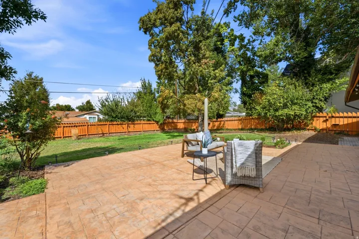 Expansive backyard oasis featuring a newly installed paver patio, mature shade trees, and lush manicured lawn bordered by wood privacy fencing