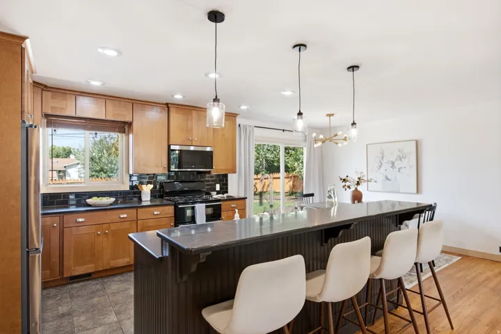 Wood-finish cabinetry with black hardware, dark tile backsplash, and stainless steel appliances