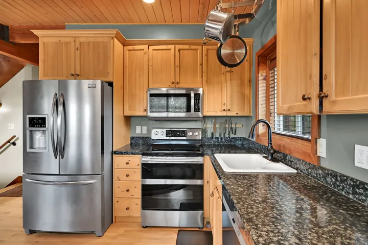 Wood-finish plank ceiling, natural wood cabinetry, stainless steel appliances, dark speckled countertops, and a white inset sink