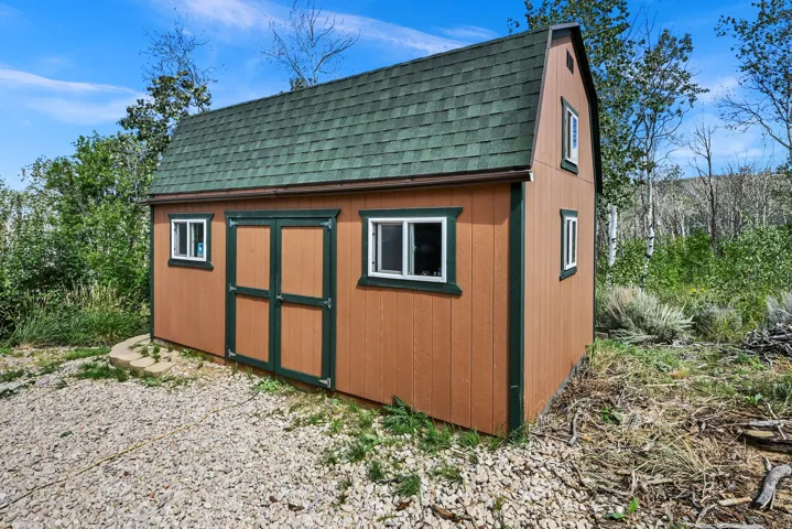 Wood-sided outbuilding with a gambrel roof and green shingles