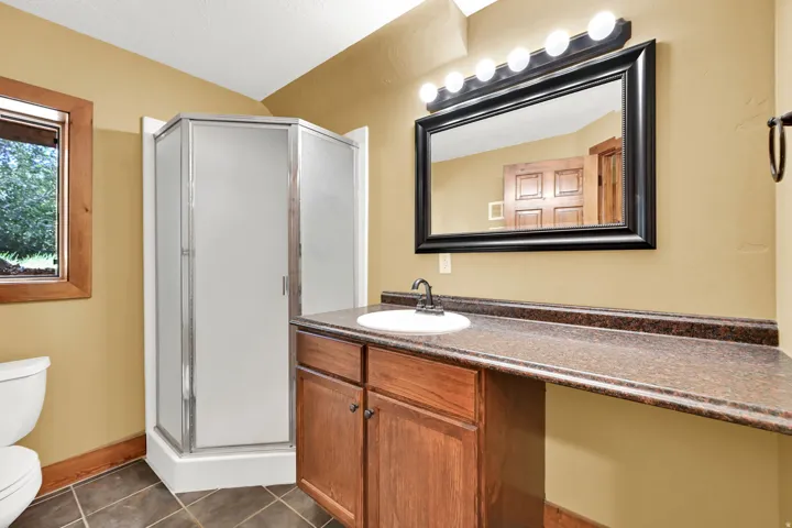 Shower enclosure with frosted panels, wood-finish vanity with an integrated sink, broad countertop, and framed mirror with overhead lighting