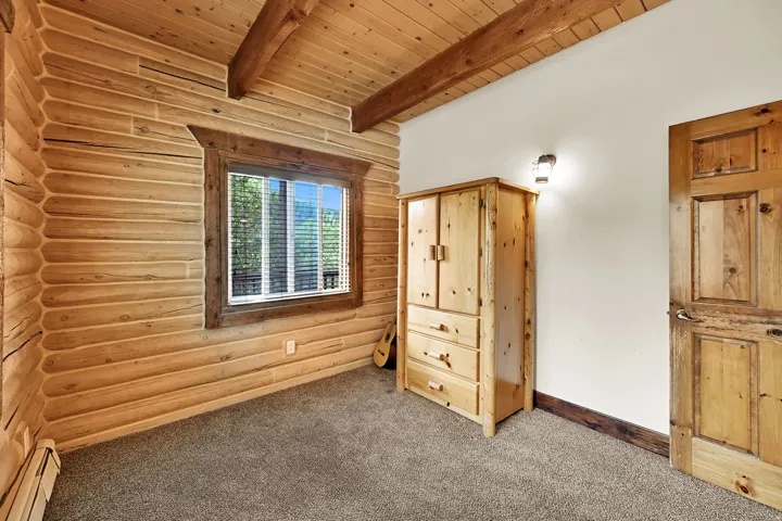 Log-style wood paneling, wood-finished ceiling, exposed wood beams, and a window with blinds