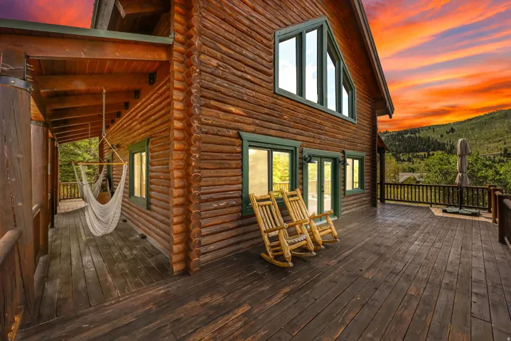Log cabin exterior with an expansive wood deck, green-framed windows, and a covered patio area
