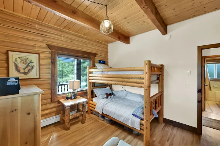 Wood-paneled walls and ceiling with exposed wood beams, wood-finish flooring, and a large window with blinds