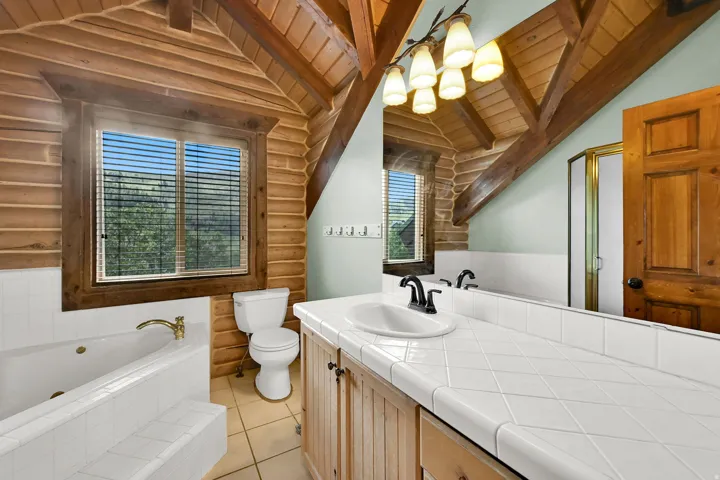 Cathedral wood-paneled ceiling with exposed beams, wood-finish walls, built-in soaking tub, wood vanity with a tile countertop, and a walk-in shower with a glass enclosure