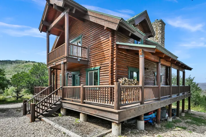 Log home exterior featuring a stone chimney, wrap-around porch, and second-level balcony