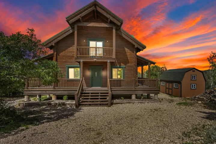 Log cabin exterior featuring a covered porch, upper-level balcony, and a detached barn-style outbuilding with multiple windows