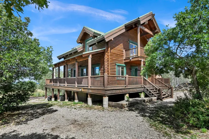 Log cabin exterior with a multi-level deck, a second-story balcony, and a gravel driveway