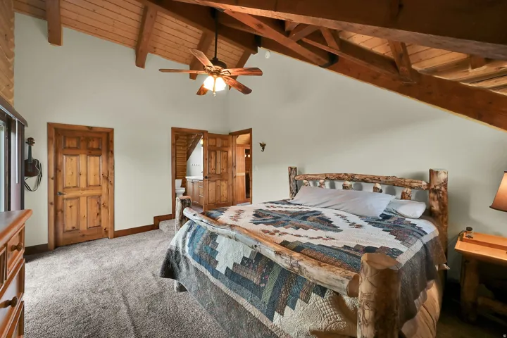 Vaulted wood-paneled ceiling with exposed wood beams, ceiling fan, natural wood doors, and carpeted flooring