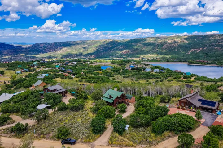 Aerial perspective showcasing multiple properties, a tranquil lake, expansive mountainous terrain, and a vibrant natural landscape