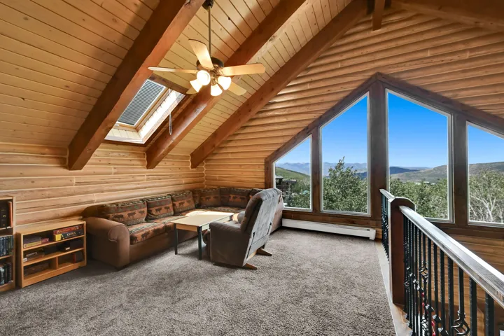 Vaulted ceilings with exposed wood beams, skylight, triangular picture windows, wood-paneled walls, and carpet flooring