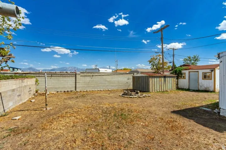 Expansive backyard featuring a concrete block perimeter wall, a shed with a shingle roof, and distant mountain scenery
