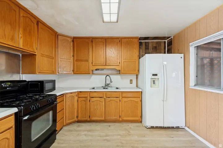 Kitchen featuring wood-finish cabinetry, white countertops, a black gas range, and wood-finish flooring
