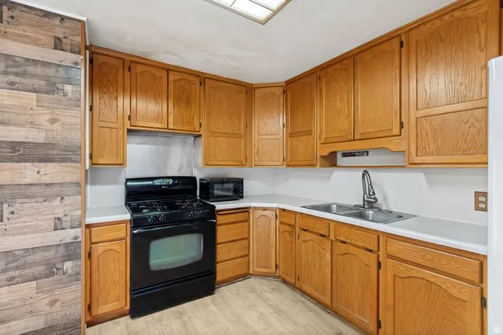 Kitchen featuring wood cabinetry, solid surface countertops, a double basin sink, and wood-finish flooring