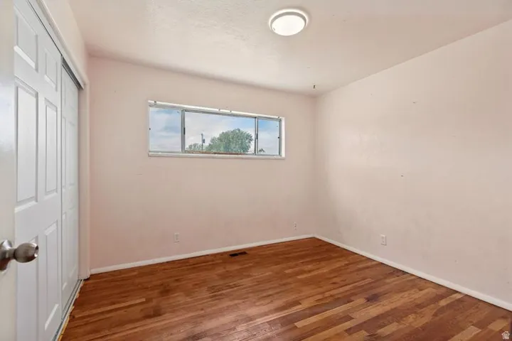 Bright secondary bedroom with warm wood-finish flooring, soft pink walls, and a transom window providing natural light