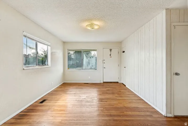 Wood-finish flooring, white paneled wall, multiple windows, interior door, and flush-mount ceiling light