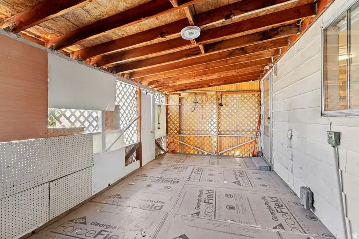 Covered outdoor space featuring exposed wood beam ceiling, lattice paneling, and a door leading to the interior