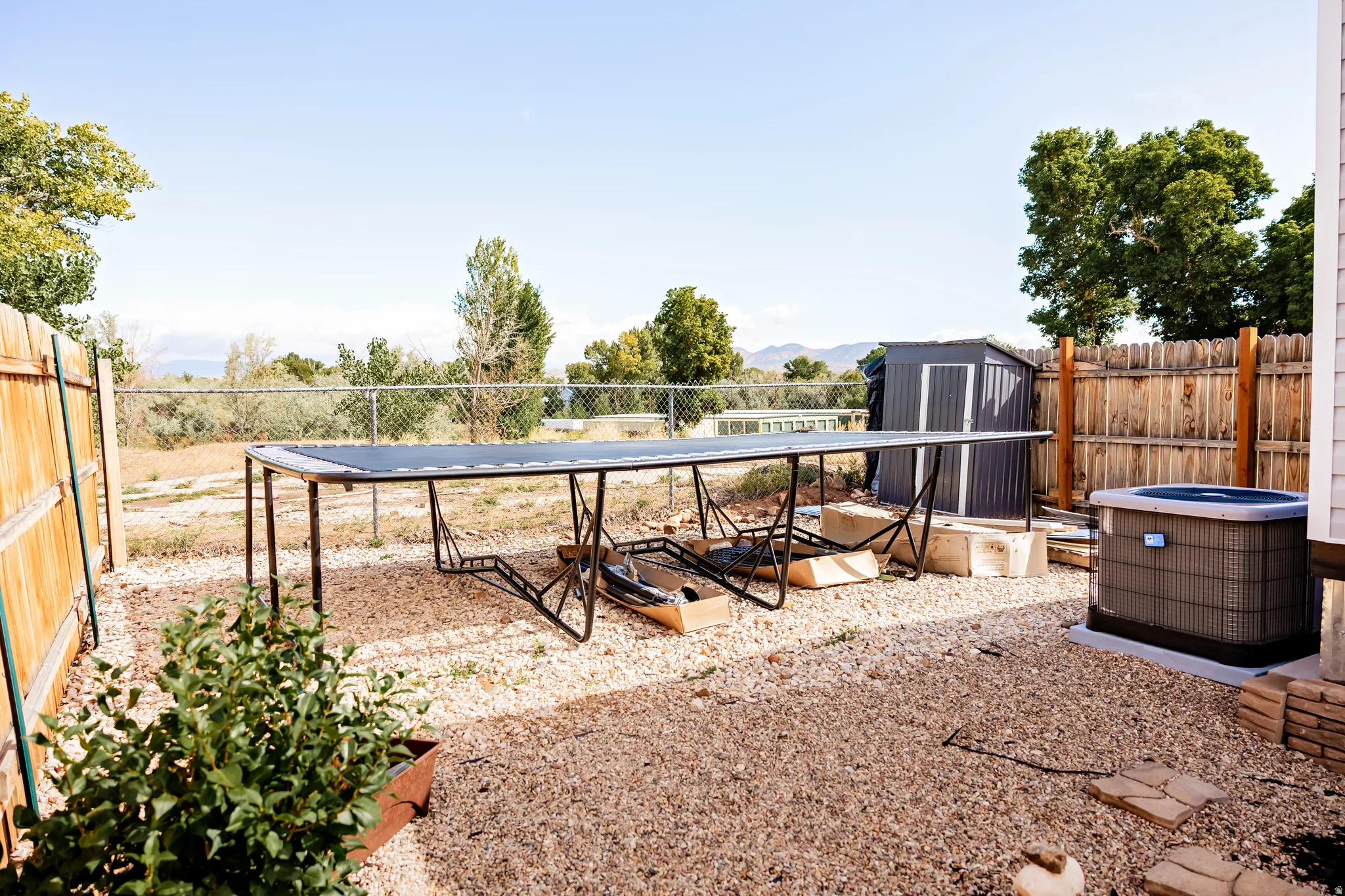 Gravel backyard featuring a privacy fence, chain-link fence, and a metal storage shed