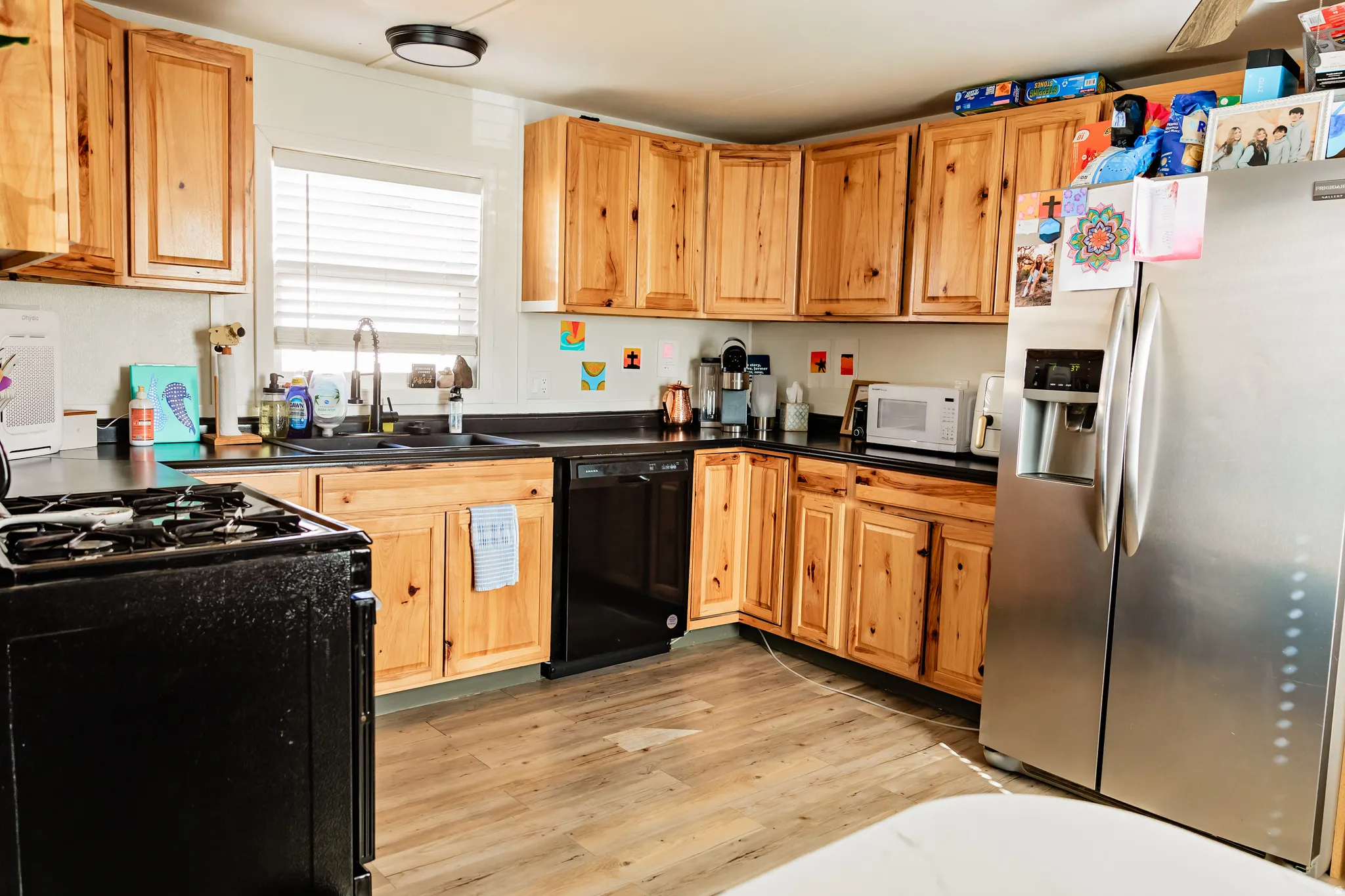 Kitchen featuring wood-finish cabinetry, dark countertops, a stainless steel refrigerator, and a black built-in dishwasher